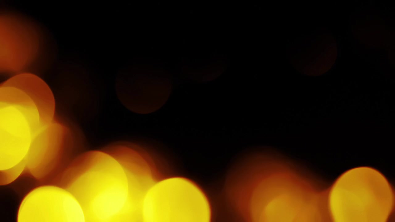 Luci bokeh calde arancioni e gialle che appaiono e svaniscono su sfondo nero