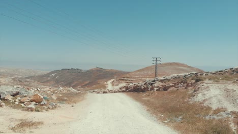 drone volando sobre un camino en una colina en el desierto con montañas alrededor, pequeños pueblos en los montes, desierto de judea, israel