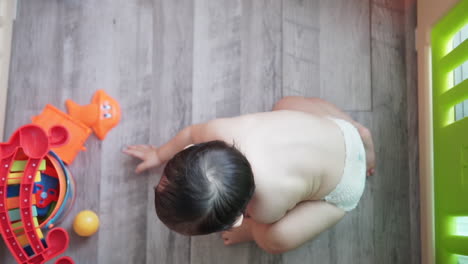 slow motion high angle shot of a one year old asian kid calmly playing by himself with colorful plastic balls and toys wearing only a diaper