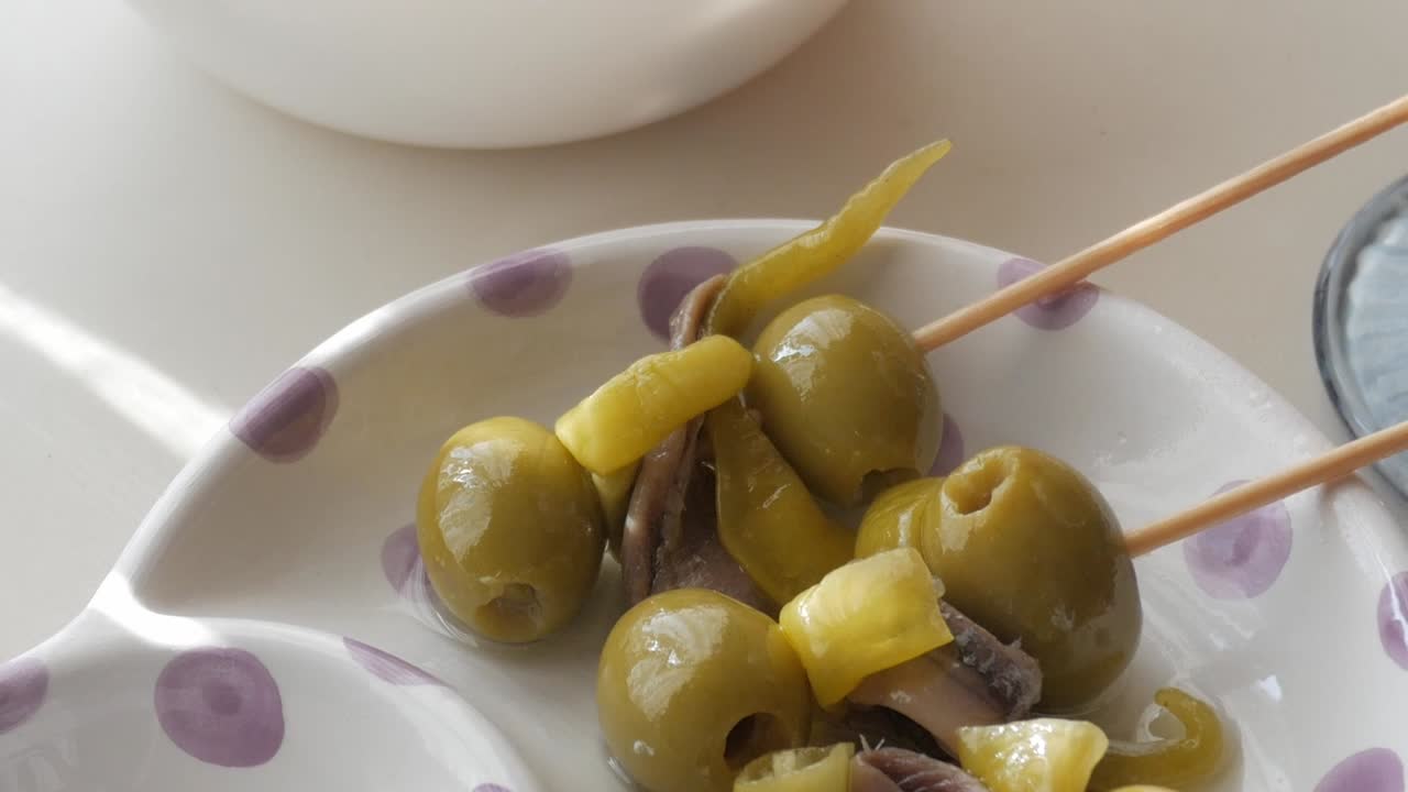A close-up of olives with anchovies and peppers skewered on toothpicks, tapas style