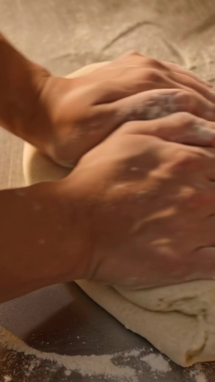 Video verticale: Mani che premono e impastano una palla di impasto su un bancone infarinato per il pane, braccia nude