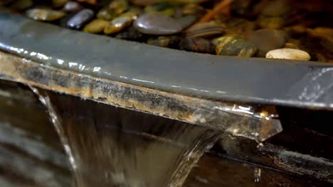 Water-fountain-with-pebbles-with-edge-seen-close-up-with-running-water,-Handheld-rotating-shot