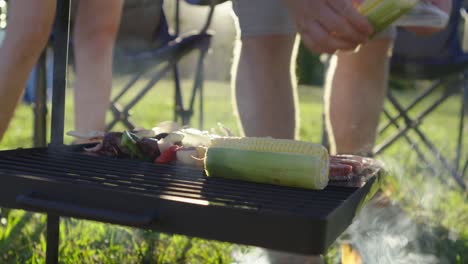 placing cobs of corn on a smokey afternoon bbq campfire