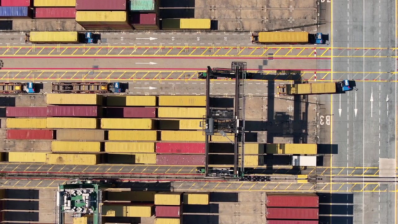 Camion portacontainer si muovono attraverso i terminal portuali. I container sono impilati su navi attraccate. Il trasporto merci subisce ritardi a causa della congestione e delle sfide operative