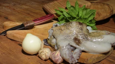 a freshly caught octopus lies on a wooden cutting board surrounded by garlic, onion, and herbs