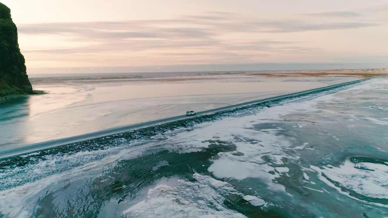 вид с воздуха за автомобилем на главной дороге рейнисфьяра, движущимся по освещенному солнцем черному песку исландского ландшафта