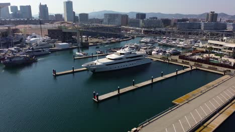 Luftaufnahme-Einer-Megayacht,-Die-Im-Hafen-Von-Barcelona-Geparkt-Ist,-Mit-Blick-Auf-Die-Stadt-Im-Hintergrund-An-Einem-Sonnigen-Tag-Per-Drohne