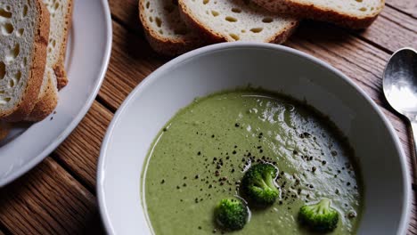 Creamy broccoli soup garnished with fresh florets, black pepper, and bread slices on rustic wooden surface, embodying wholesome culinary comfort