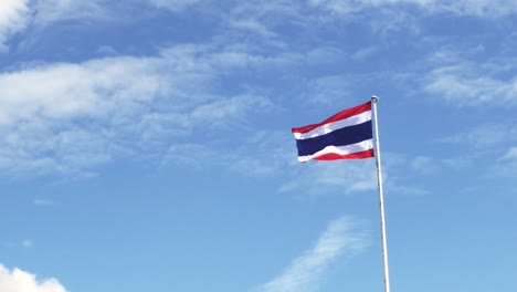 waving the kingdom of thailand flag on a pole with blue sky and white clouds in the background