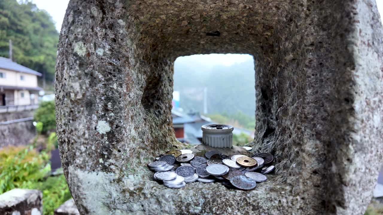 Coins placed in a stone lantern amidst an overlooking view of a Japanese village. push forward shot