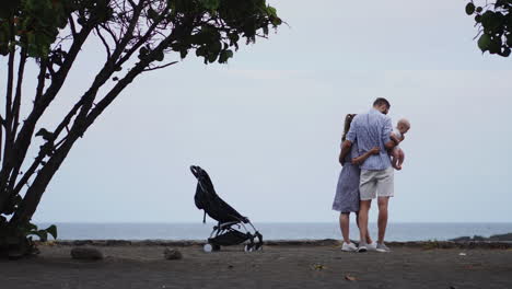 Con-El-Sol-Iluminando-Su-Camino,-Una-Joven-Familia-Caucásica-Contenta,-Incluido-Su-Hijo-De-Un-Año-En-Un-Cochecito,-Camina-Tranquilamente-Por-Un-Embarcadero-De-Madera.