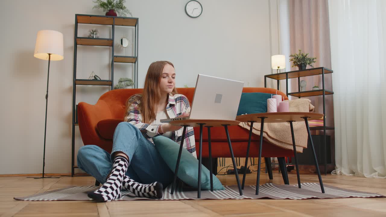 Cheerful young woman sitting on floor using laptop pc share messages on social media application