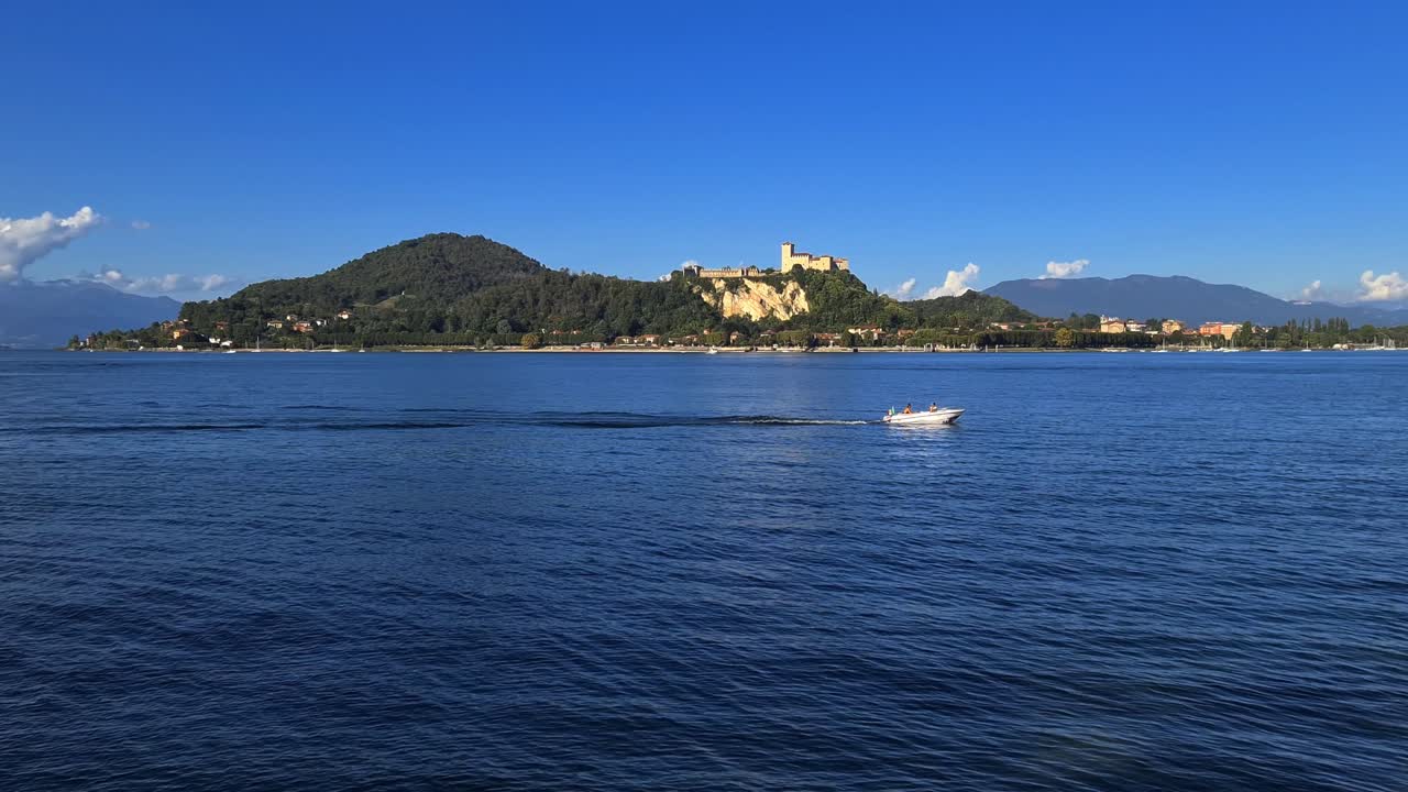 Piccola barca a motore che naviga nelle acque calme del Lago Maggiore in Italia, con il Castello di Angera sullo sfondo.
