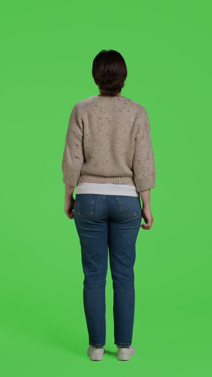 Vertical video: Back view of young adult doing thumbs up symbol on green screen