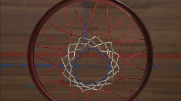 Un giocatore di basket si appende al canestro dopo che la palla è passata, poi scende e si allontana.