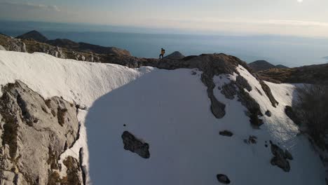 Man-walking-on-top-of-rocky-snowy-mountain,-Sveti-Jure,-Park-Prirode-Biokovo