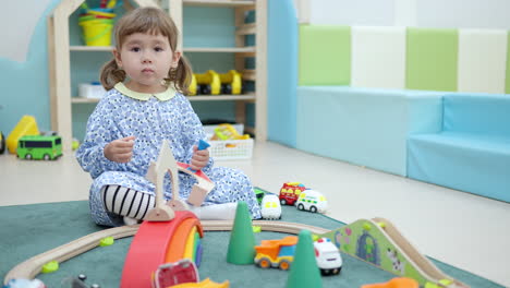 curious little girl with pigtails playing with toys and looking out what other kids do on a floor at playroom