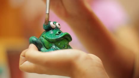 Potter-at-work.-Closeup-female-hands-painting-green-ceramic-frog