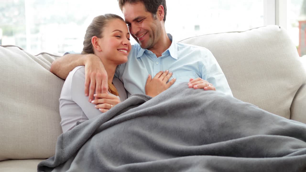 Cute couple lying on couch chatting under a blanket