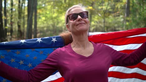 mujer bonita y rubia mirando a la cámara y sonriendo sin quitarse una bandera estadounidense que la envuelve