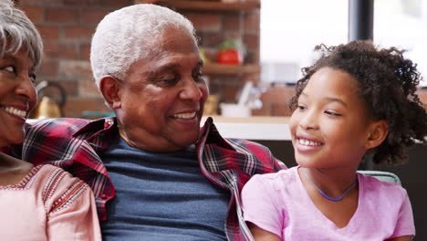portrait of grandparents sitting on sofa at home with granddaughters