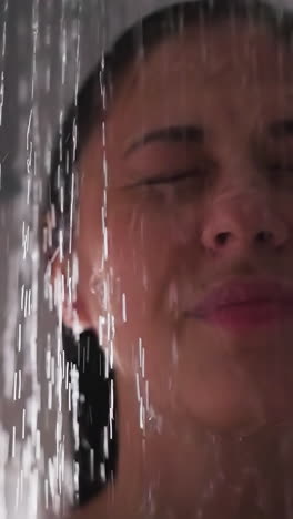 happy woman with water pouring down face in shower closeup. positive lady with closed eyes enjoys spa procedures in bathroom. hygienic routine