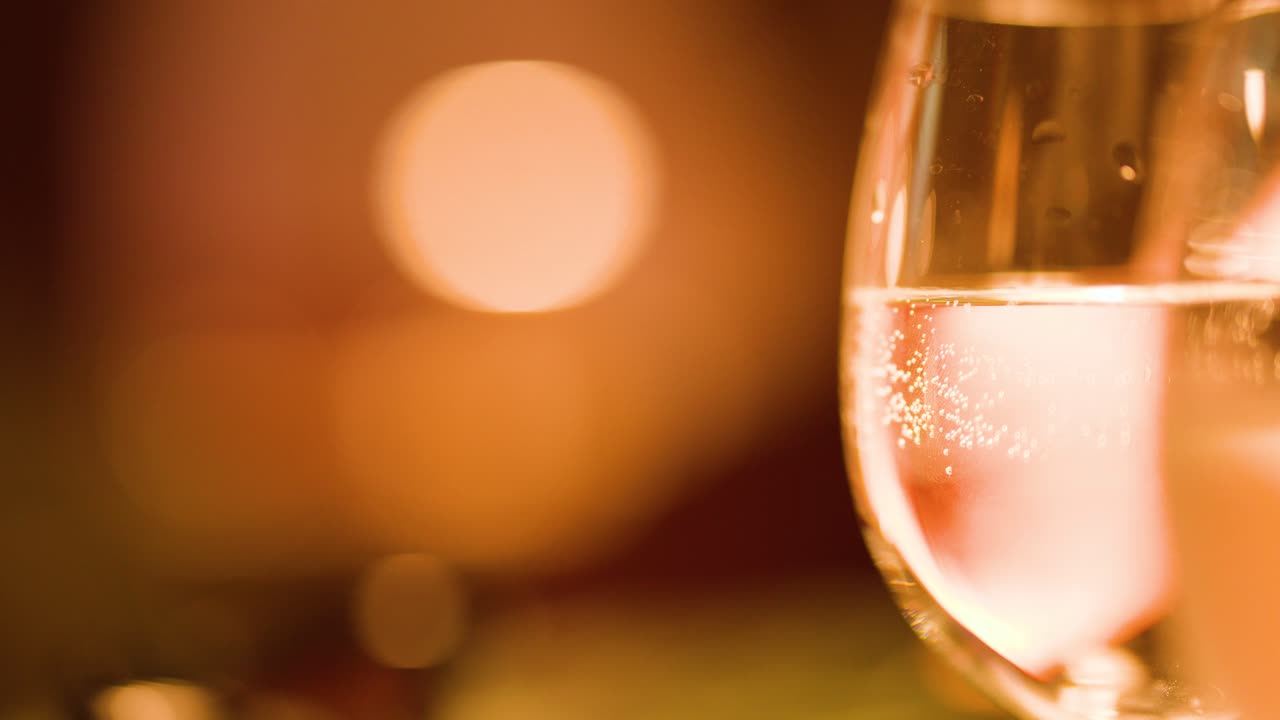 Macro di un bicchiere d'acqua frizzante con luci bokeh, illuminazione ambientale calda e messa a fuoco selettiva