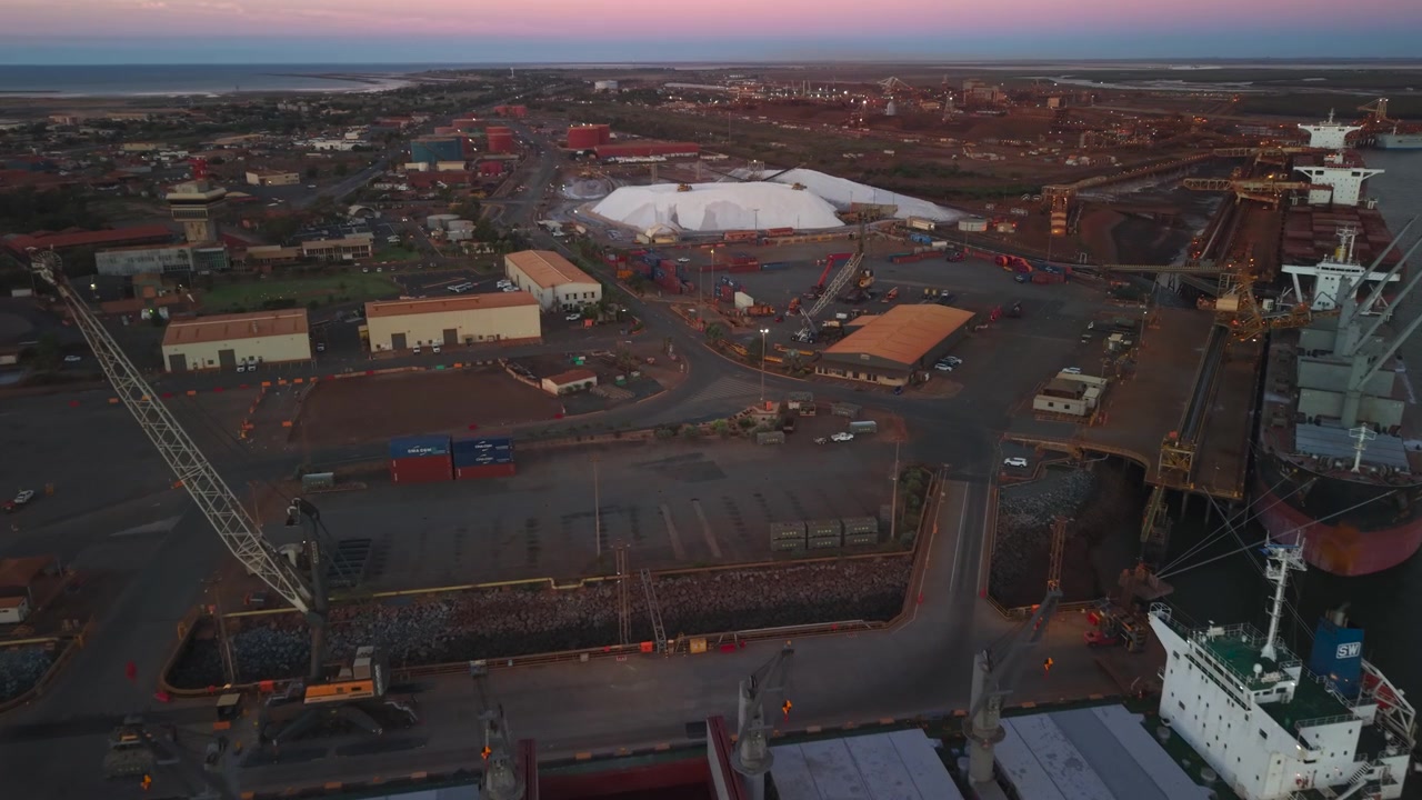 Ships are docked while xcavators load raw material onto conveyors for shipping in the background port hedland australia