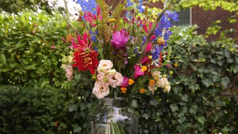 colourful wedding flowers in clear vase with green hedge in background