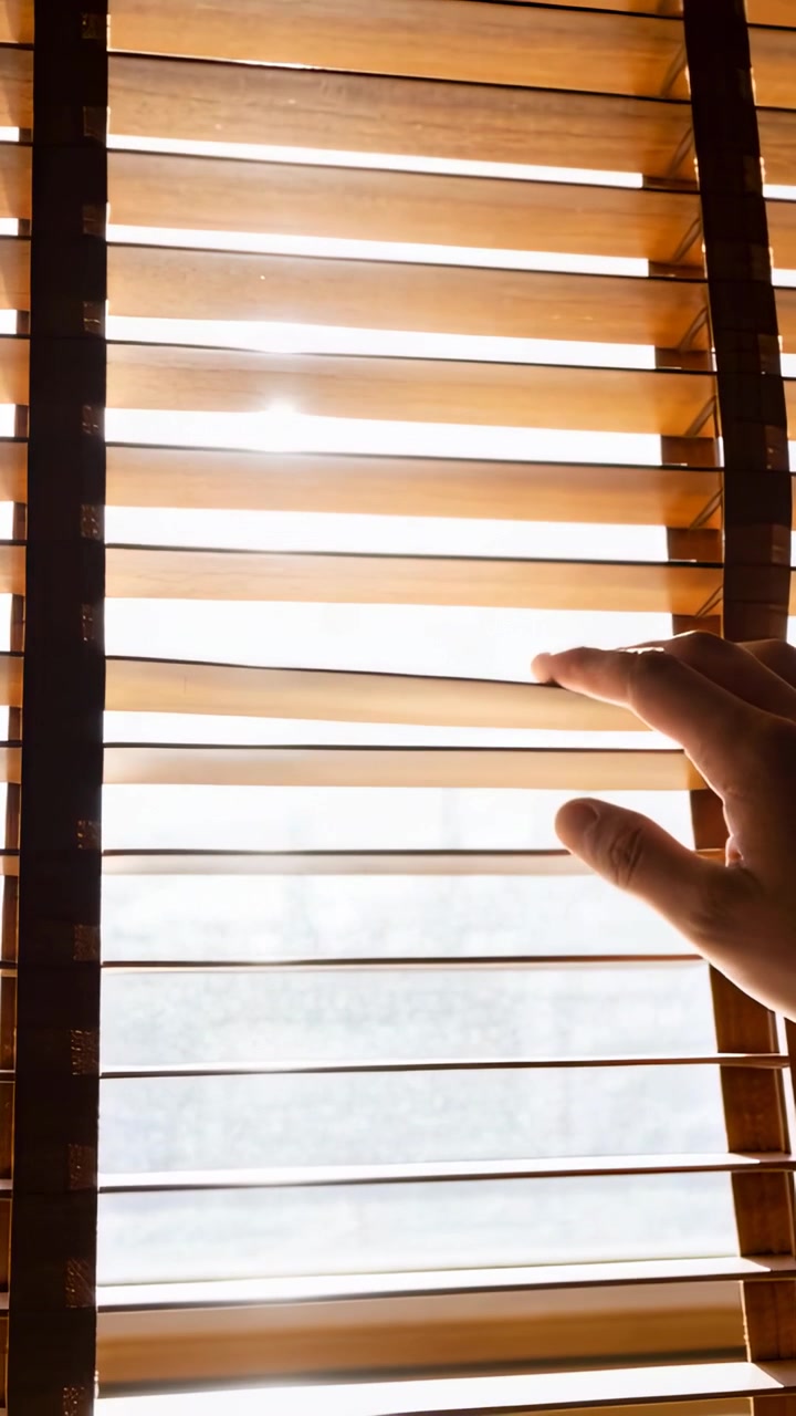Vertical video: Reaching right hand opening wooden blinds at home, letting light in, copy space