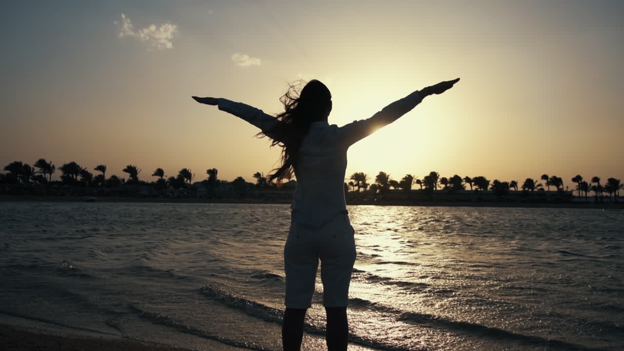 una chica feliz de pie en una playa de arena, una mujer feliz pasando el amanecer en la orilla del mar.