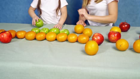 mother and daughter playing with fresh fruits at home. child and a female putting ripe fruits on the table. organic food concept.