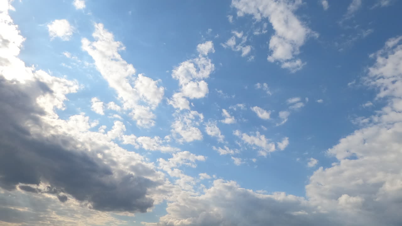 Sunny blue skies with light white clouds flying by the horizon. Big grey cloud approaches and covers the sky. Timelapse.