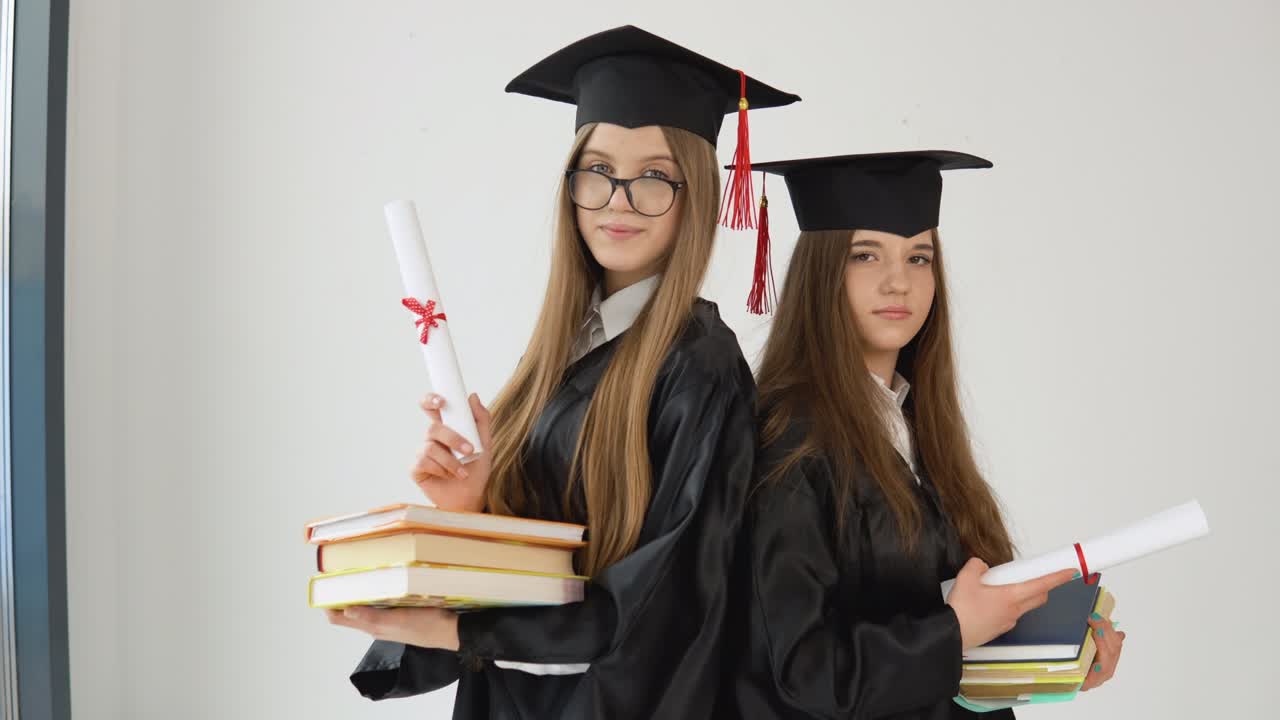 две молодые счастливые выпускницы стоят плечом к плечу с дипломами и книгами в руках.