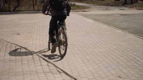 vista cercana de un ciclista de pie al lado de una bicicleta en un camino pavimentado para montar, el ciclista está usando una chaqueta y pantalones vaqueros, con la sombra de la bicicleta echada en el suelo