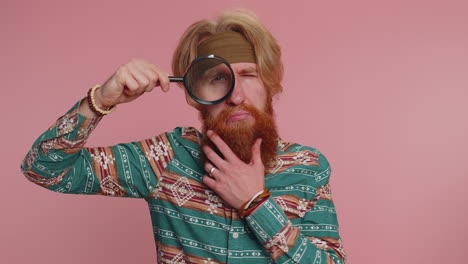 man with a red beard looks through a magnifying glass and winks