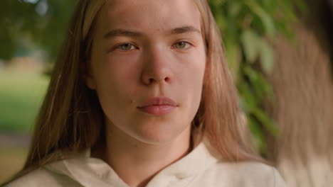 close-up of young woman looking intently with gentle sunlight reflecting on her face, creating a peaceful expression, while blurred greenery and gently swaying leaves fill the background