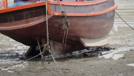 Un-Primer-Plano-De-La-Popa-De-Un-Barco-De-Pesca-Tradicional-Tailandés-Amarrado-Y-Varado-Durante-La-Marea-Baja-En-Tailandia