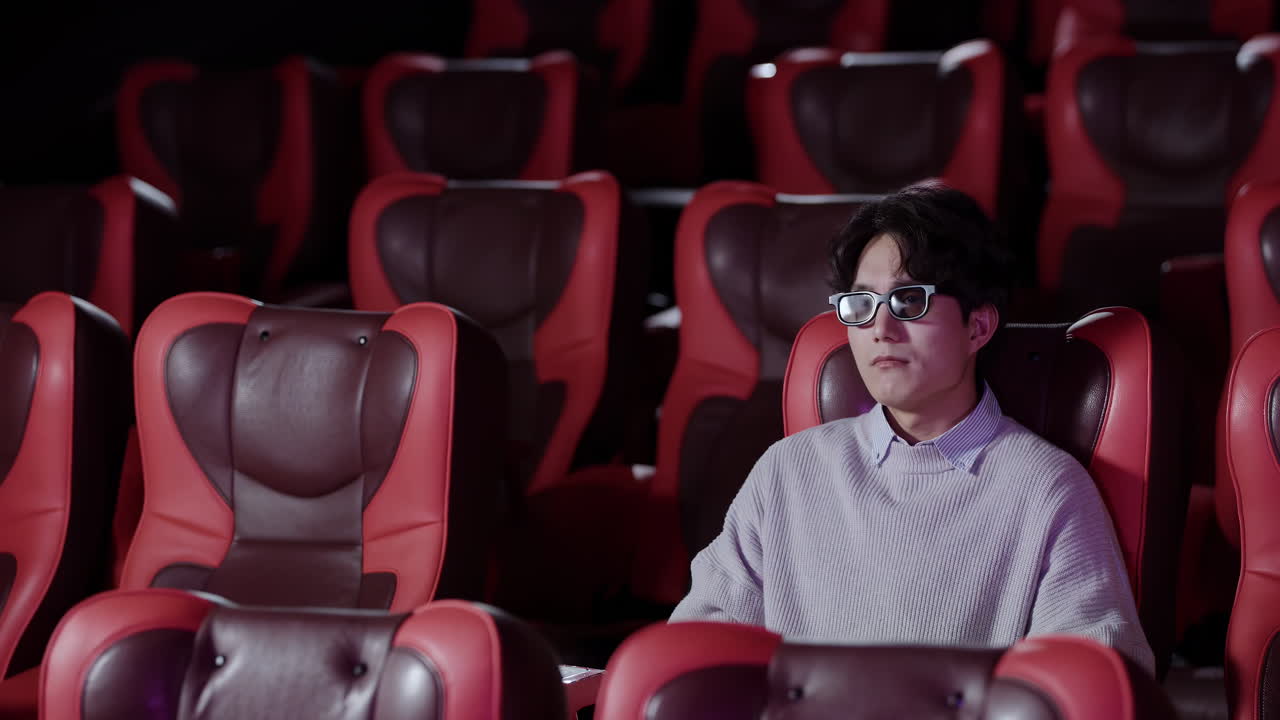 Ritratto di un giovane spettatore solitario che guarda intensamente dal suo posto, godendosi un film al cinema, seduto da solo in un auditorium vuoto, emanando un senso di svago e intrattenimento.