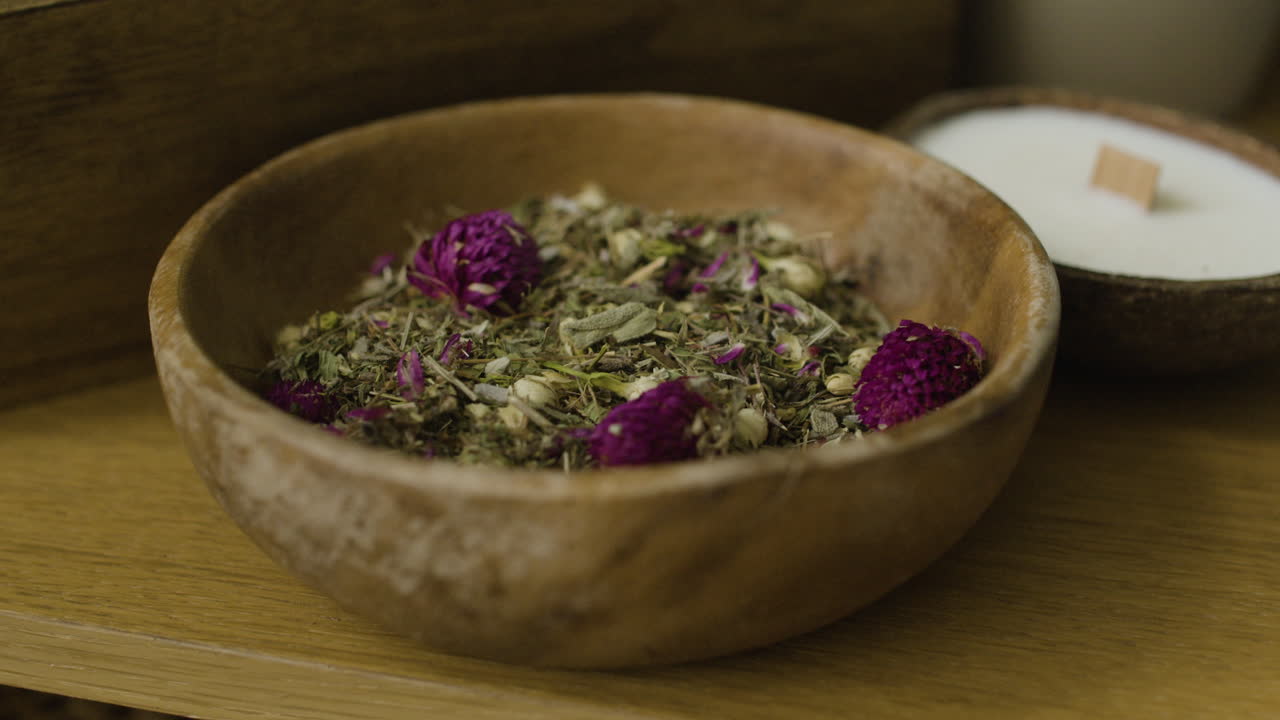 A bowl of dried herbs and flowers next to a candle