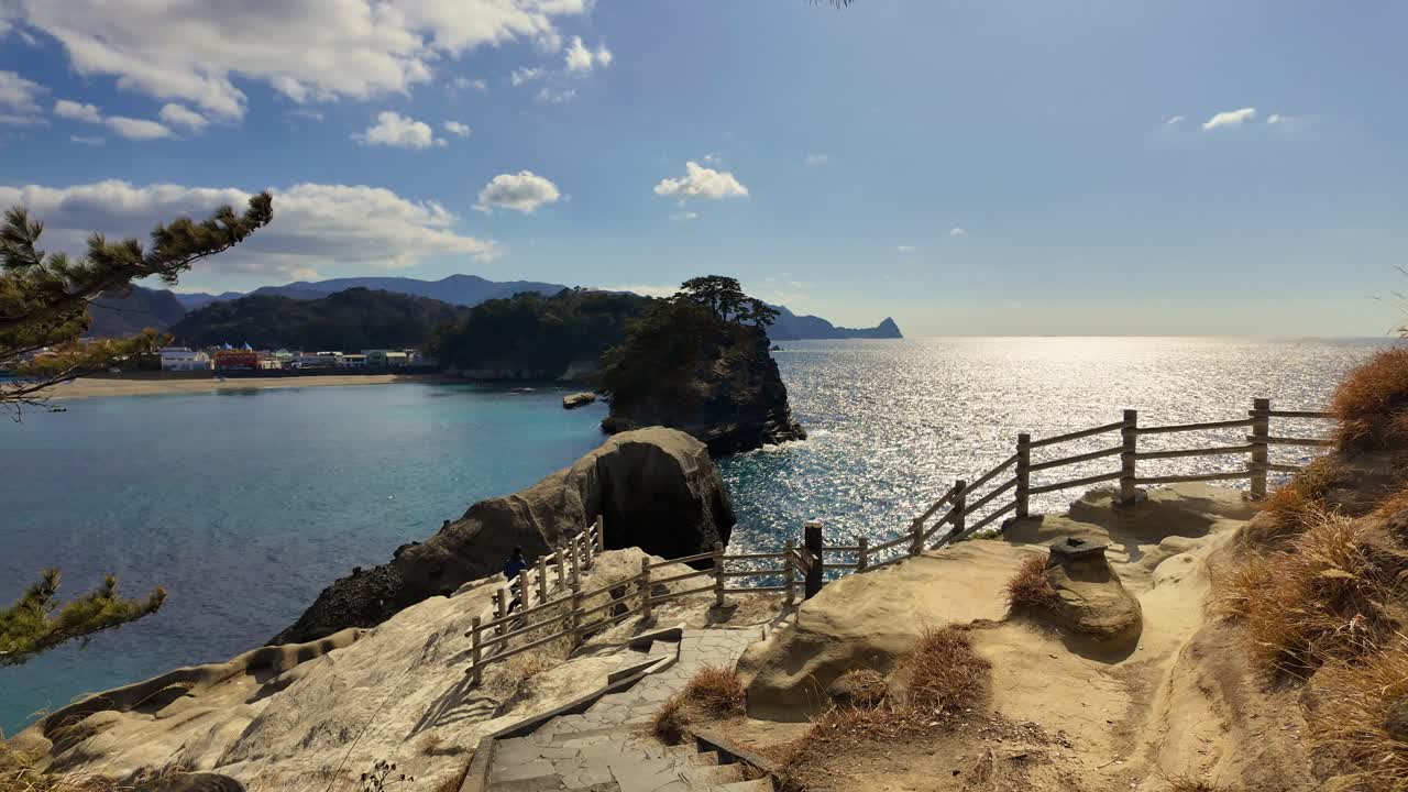 Una vista panorámica desde un área de descanso hacia la impresionante costa de Dogashima, mostrando la icónica cueva marina de Tensodo, la bahía azul y las islas rocosas bajo un sol brillante