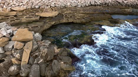 aerial erial view over a rocky shore line with traditional salt pans and waves splashin in slow motion