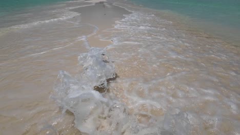 tilt up waves crash on tropical white sandbank, people enjoy beach in background