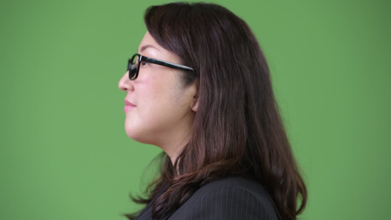 Rear view of mature beautiful Asian businesswoman looking back against green background