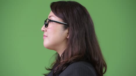 rear view of mature beautiful asian businesswoman looking back against green background