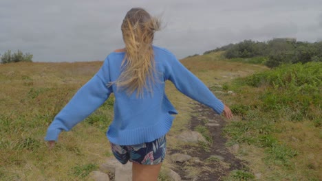 caucasian woman walking towards end of big nobby peninsula on a windy morning - crescent head lookout, nsw, australia