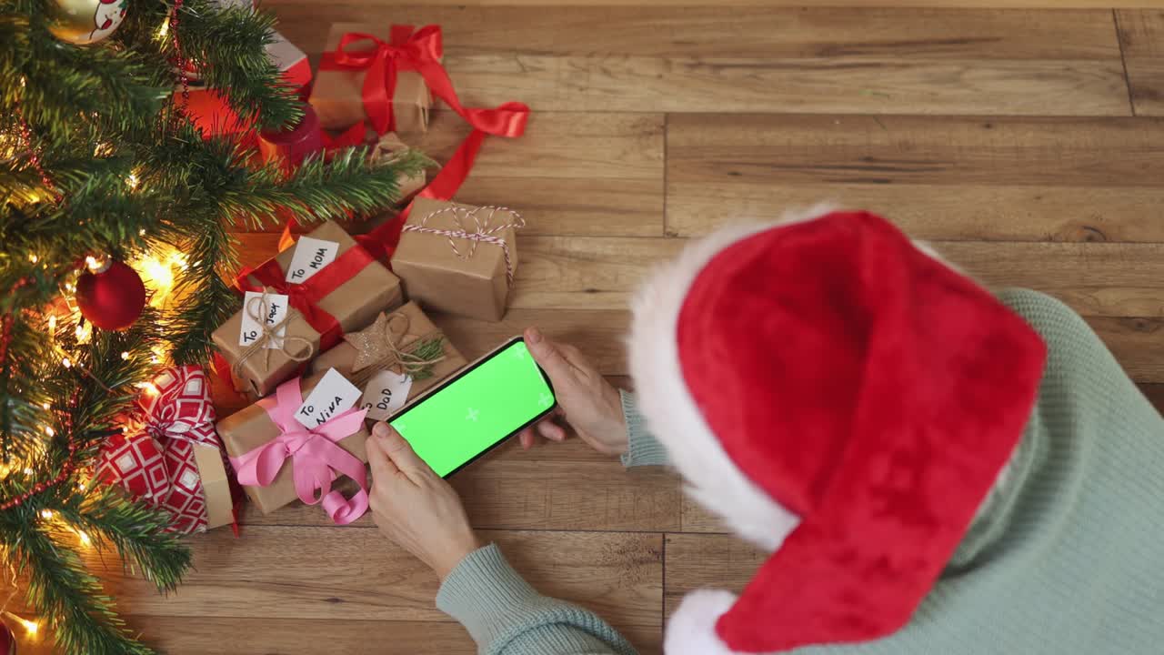 sombrero de navidad rojo femenino manos de teléfono inteligente pantalla verde bajo cajas de regalos de abeto