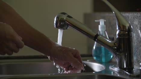prevención del coronavirus hombre enciende la faceta, aplica jabón azul y se lava las manos con agua corriente en el fregadero