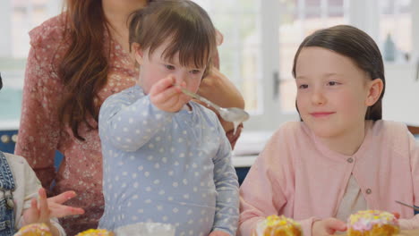 mother with down syndrome daughter baking and decorating cakes sitting around table at home