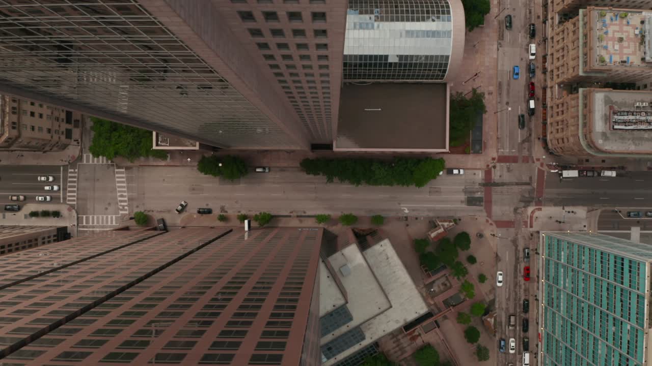 Vista aérea de uma rua larga e movimentada no centro de Dallas, Texas, EUA, ladeada por altos edifícios comerciais. Imagem com movimento panorâmico horizontal.